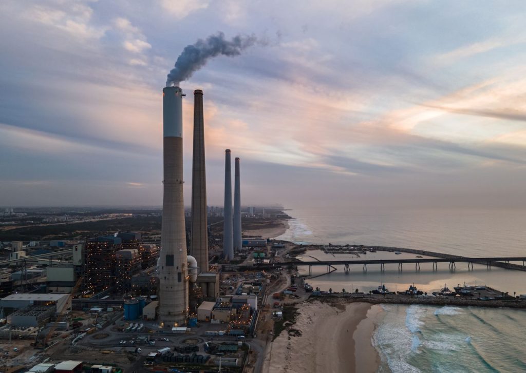 Service Aerial view of an industrial plant by the ocean with smoke stacks at sunset, capturing an industrial and serene contrast.